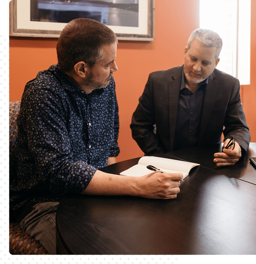 Two professional men gathered around a table reviewing notes.