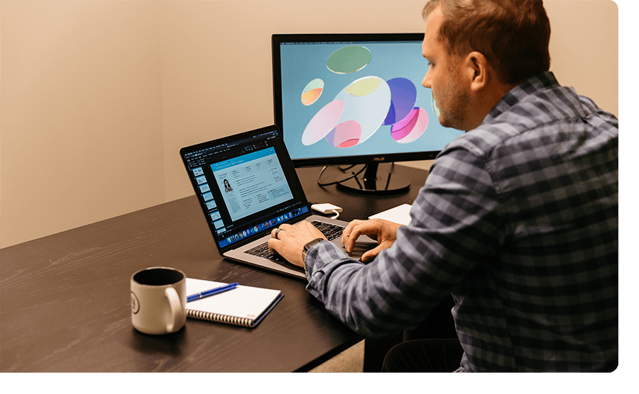 Man with brown hair and a plaid shirt working on a laptop.