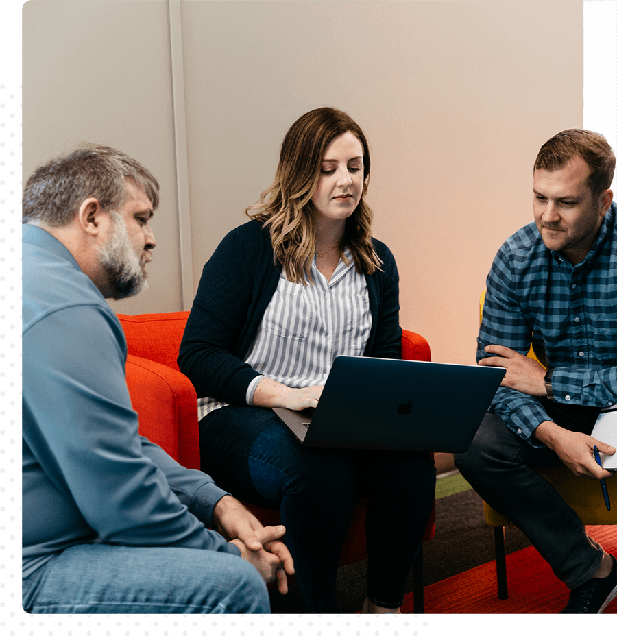 Three coworkers sit together looking at a laptop.