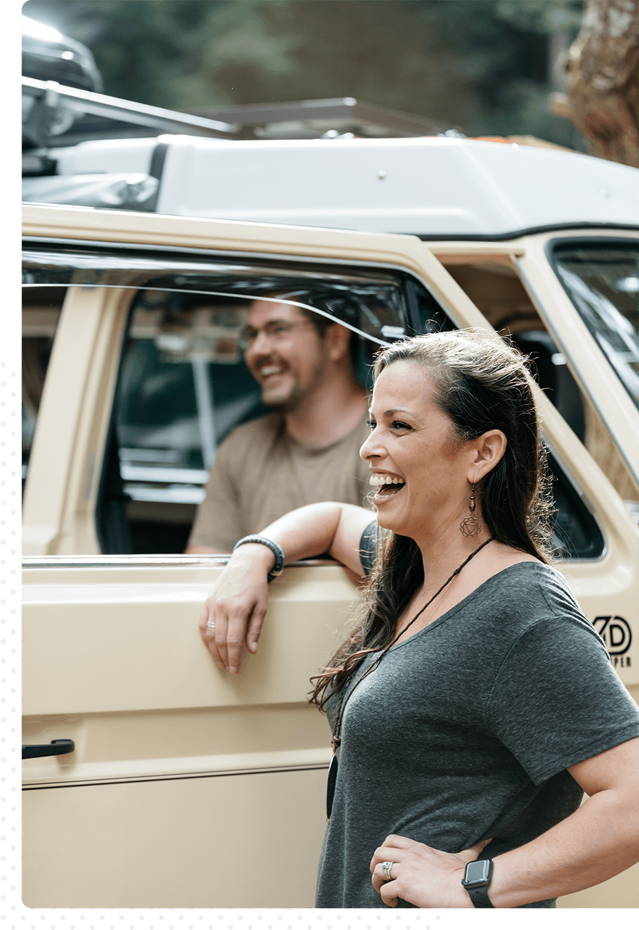 A laughing woman with her arm on the window of a van with a man inside.