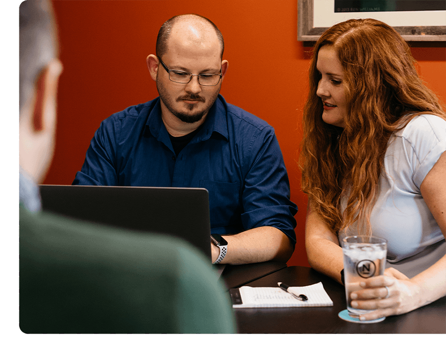 Two people sit together at a black table looking at a computer.