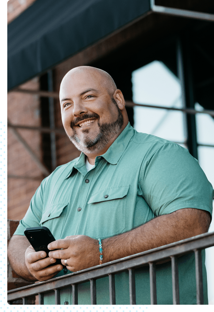 A man stands outside smiling with his phone in his hands.