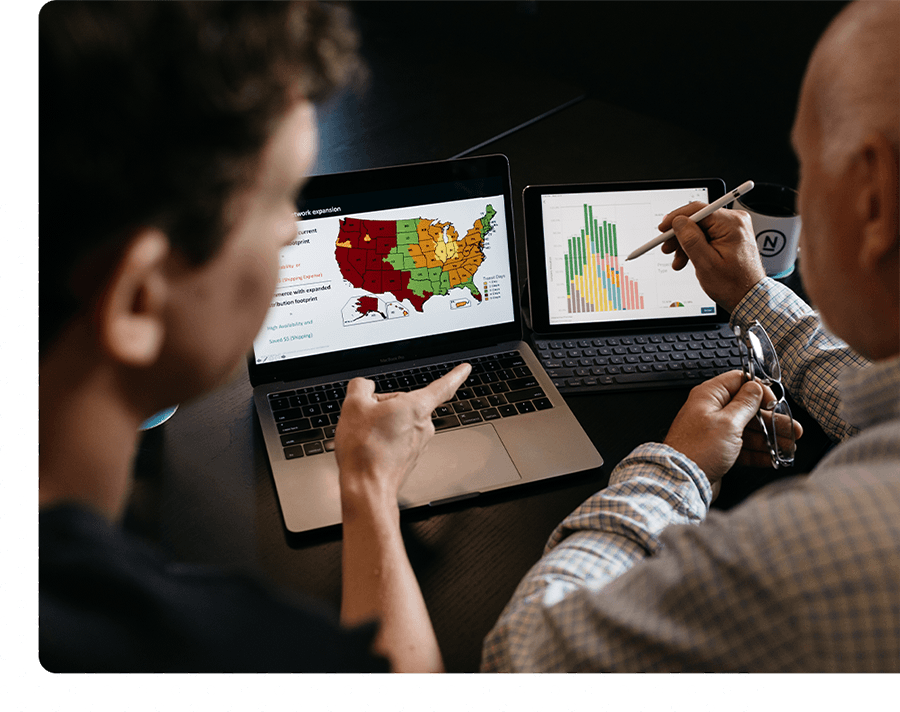 Two people sit together pointing to data on their laptop.