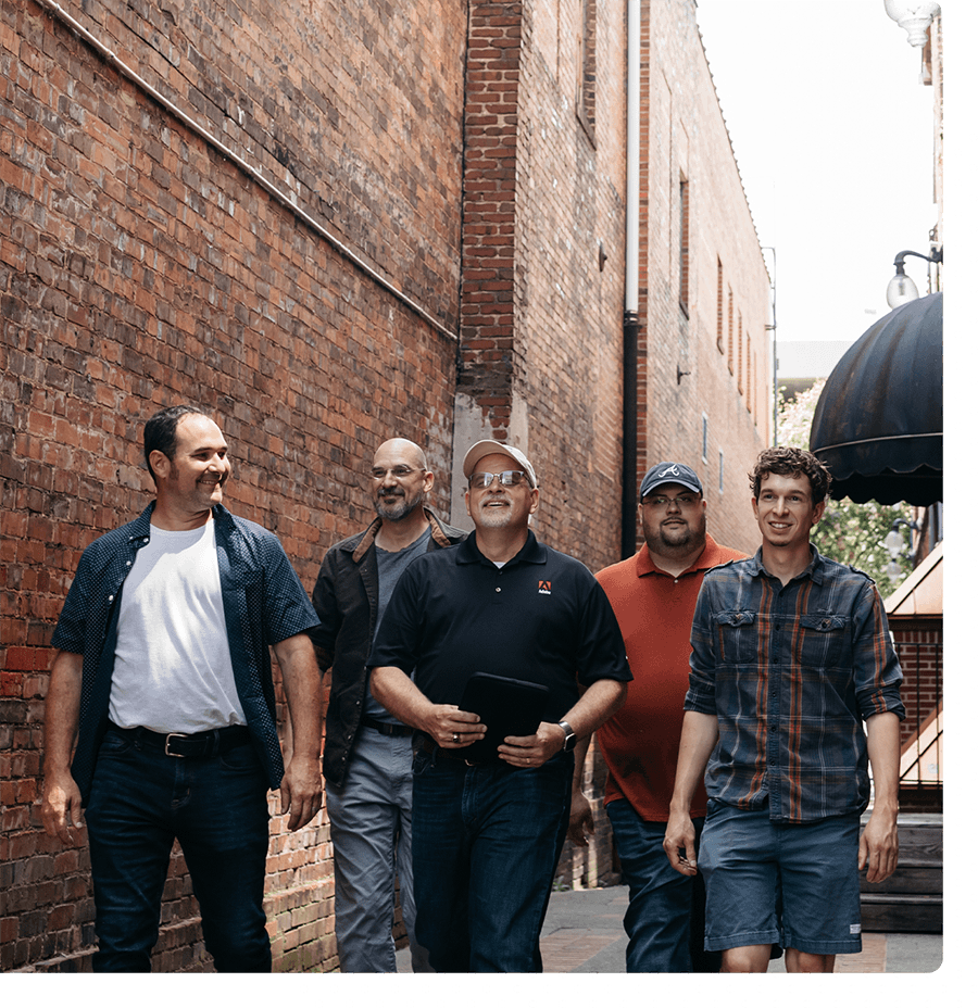 A group of five mean dressed casually walking down a street with brick buildings