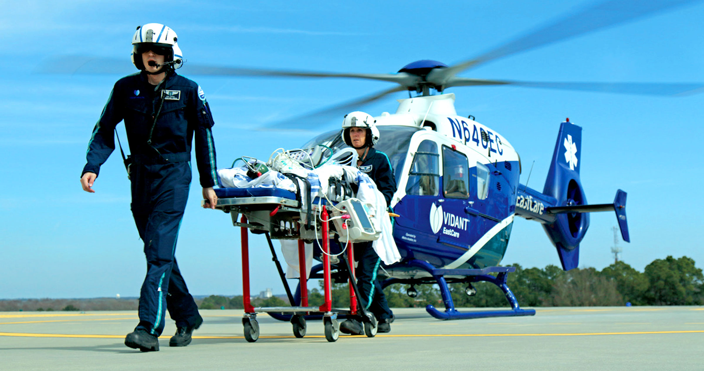 Two emergency response crewmen take a patient off a helicopter and walk towards hospital.