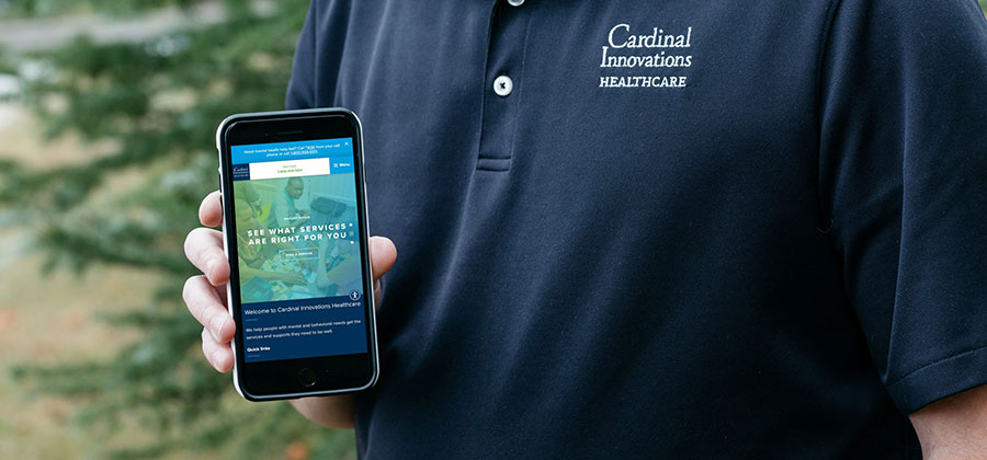 A cropped image of a man holding a mobile phone with the Cardinal Innovations website pulled up.