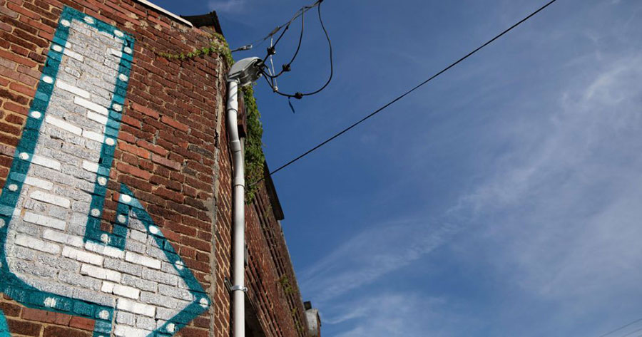 An image of a white and blue arrow painted on a brick wall. The sky is blue in the background. Downtown Johnson City.