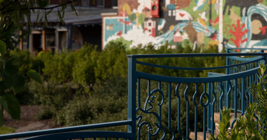 An image of a green wrought iron fence with a park and colorful wall mural in the background. Downtown Johnson City.