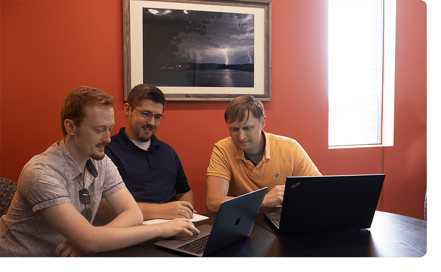 Three men in polos working on laptops in an orange room.