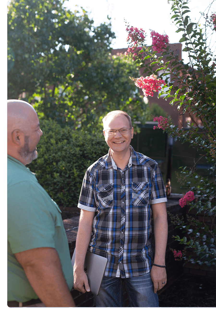 Two men stand outside talking. There is a tree with pink blooms behind them.
