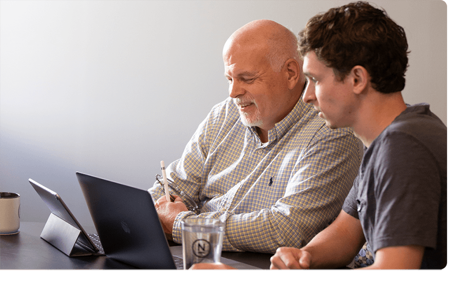 Two employees look at their laptop together.