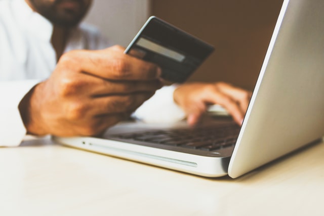 A man's hands holding a credit card, buying something online on his laptop.