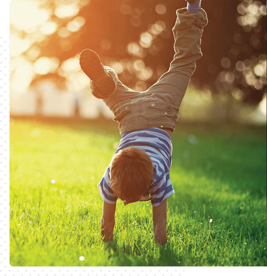 A small child plays outside in the grass. He is doing a handstand.
