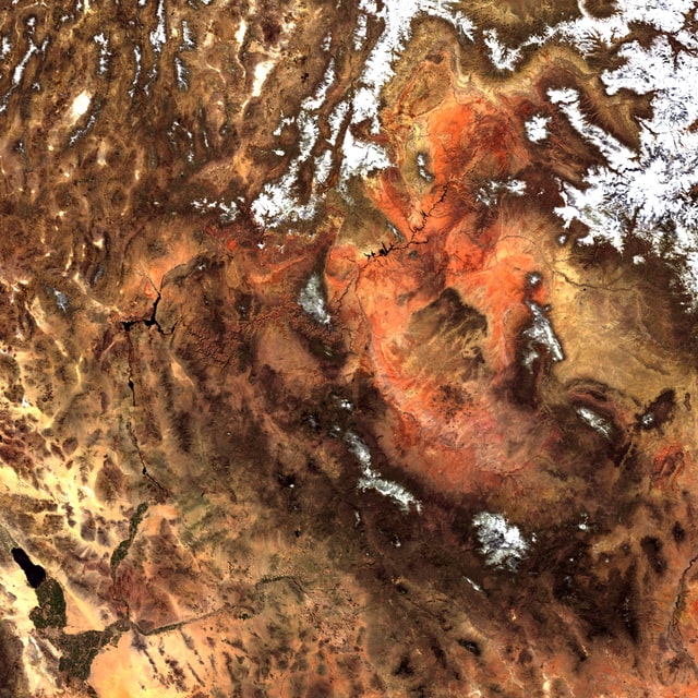 A photo from a satellite in space looking down on a desert of brown, orange, and tan with some white snow patches.