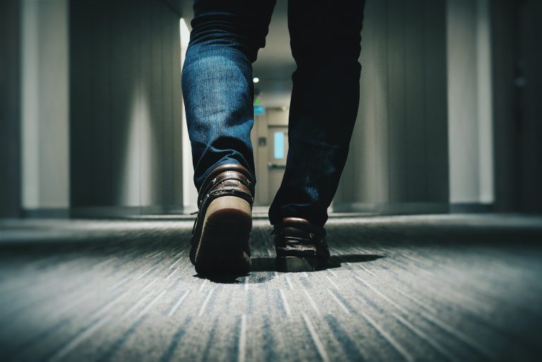 A close up view of a man in jeans and brown loafers walking down an office hallway.