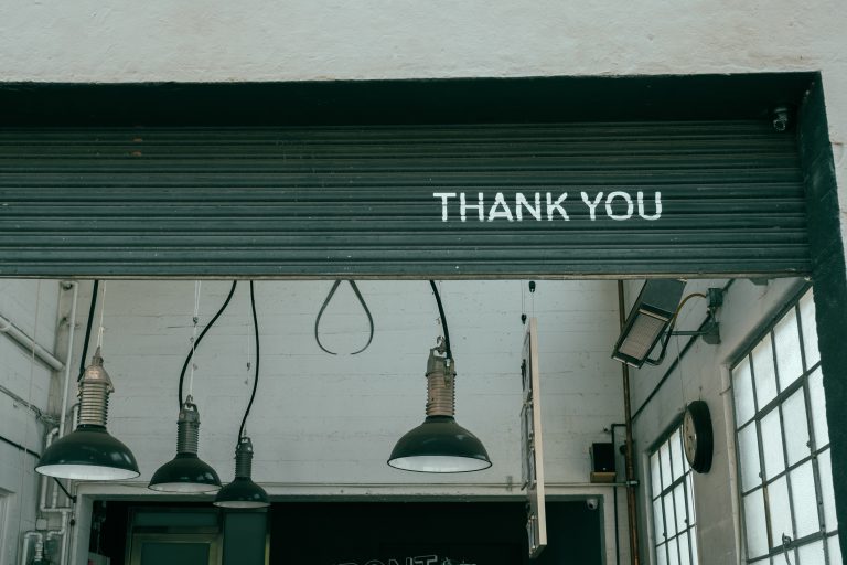 A warehouse garage door is rolling up. The bottom of the door says, "Thank you".