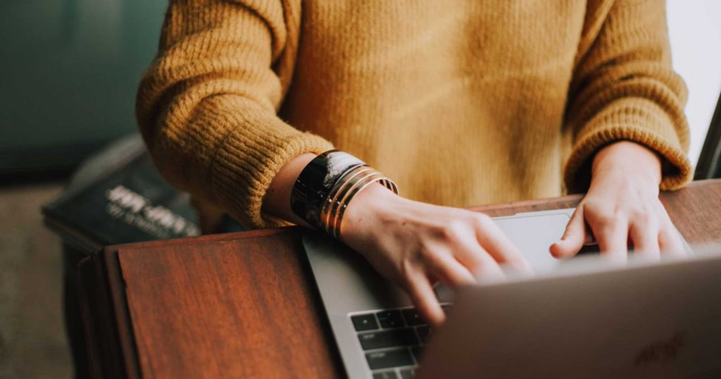 A person in a yellow sweater typing on a computer.