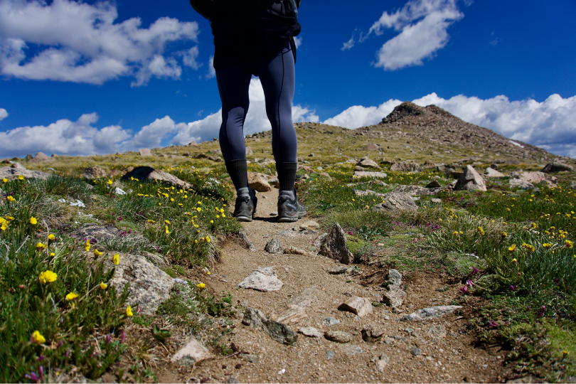 Woman hiking up grassy hill in summer time. 