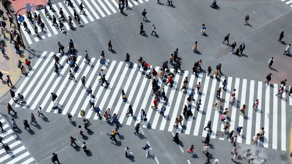 A crowd of pedestrians walking through cross-walks in a busy city.