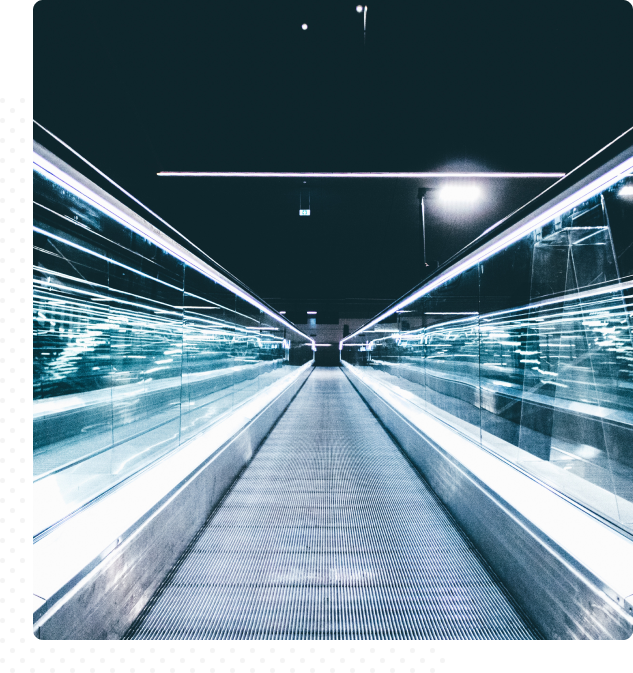 Group 148(4) Abstract image of a moving sidewalk. On either side are glass walls that reflect light.