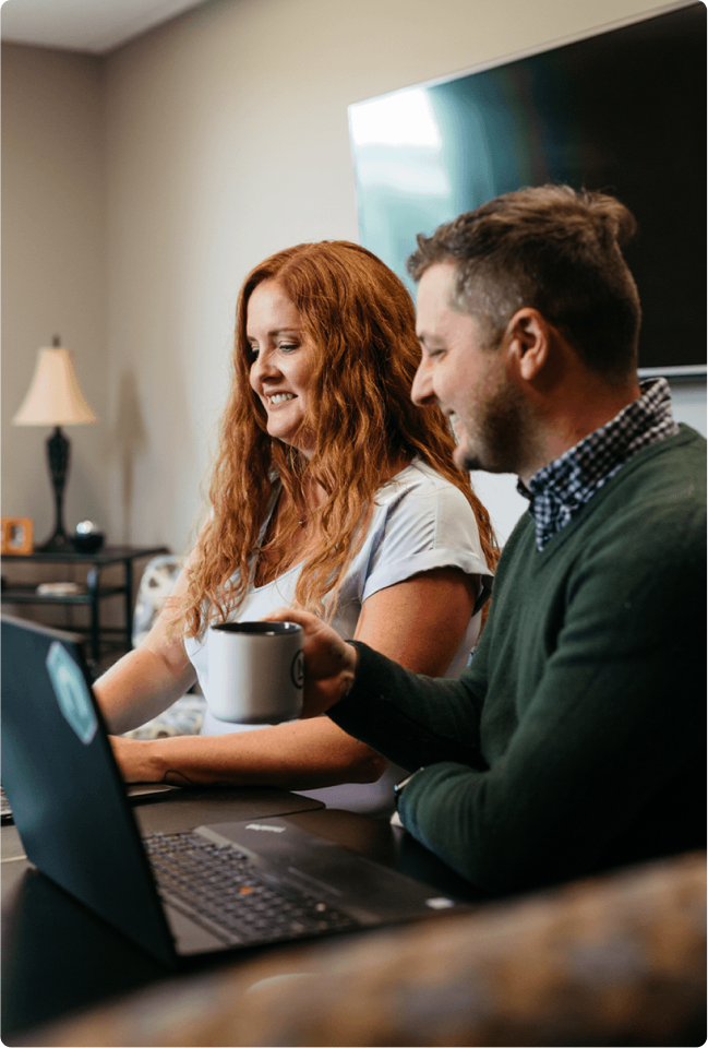 linkedin-sales-navigator-hrhjn6ZTgrM-unsplash 1(2) Man and woman sitting at a computer smiling. Man is drinking coffee.