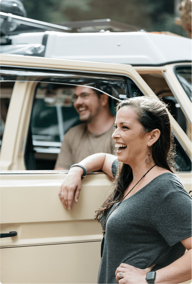 linkedin-sales-navigator-hrhjn6ZTgrM-unsplash 1(7) Man and woman laughing. Woman stands outside of a beige van with her elbow on the open door frame. Man with glasses sits inside the van.