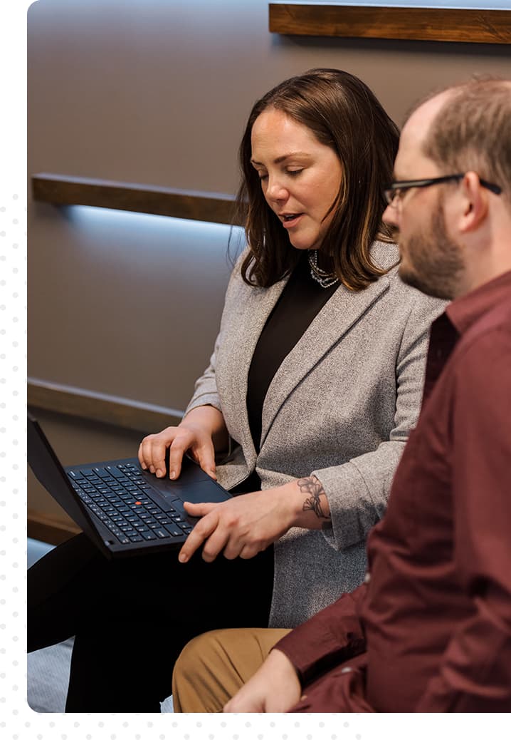 Image of a woman, seated, holding a laptop, while a man, also seated, looks at her screen.