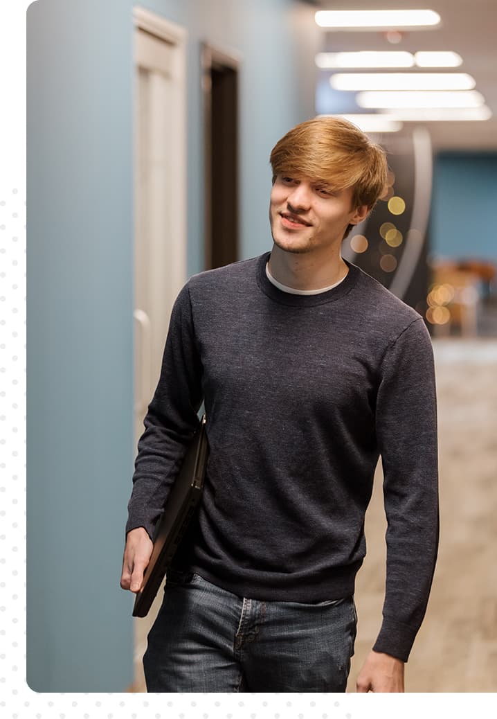 photo of smiling man walking down a hallway holding a computer