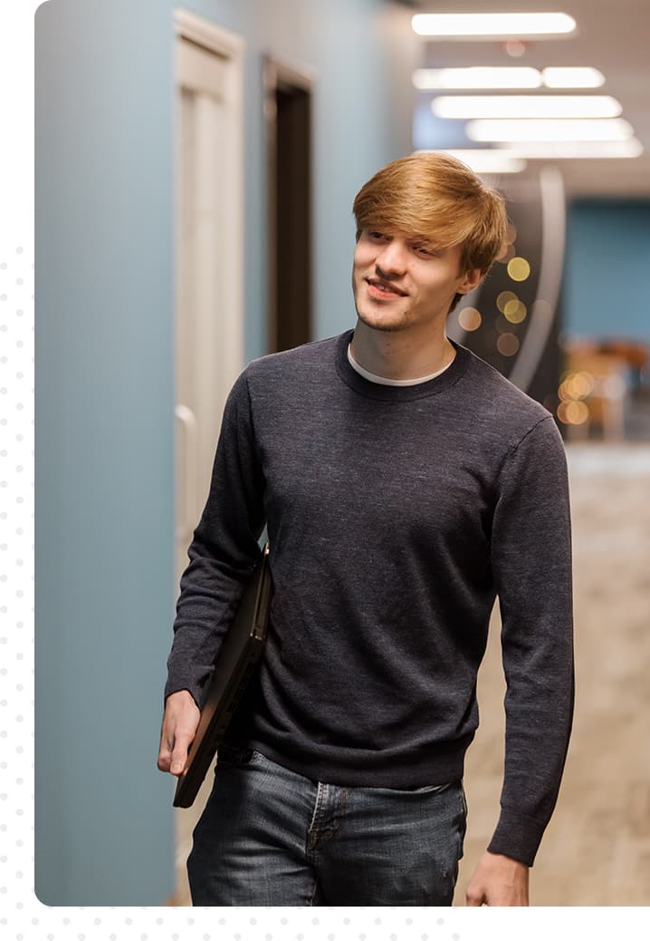 photo of smiling man walking down a hallway holding a computer 