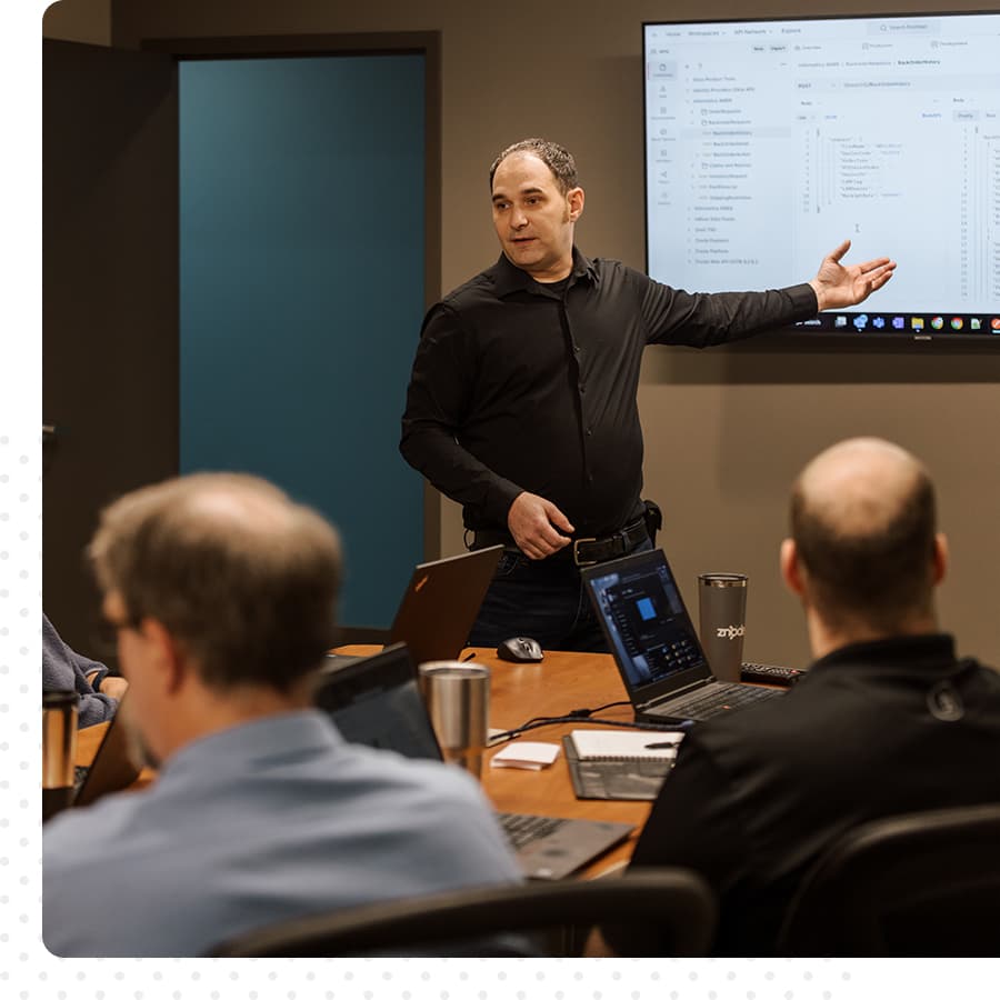 Man in a black shirt, presenting to group, gesturing to screen.