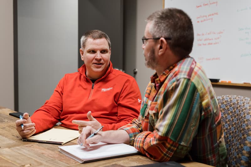 Two men sitting at a table, talking and taking notes.