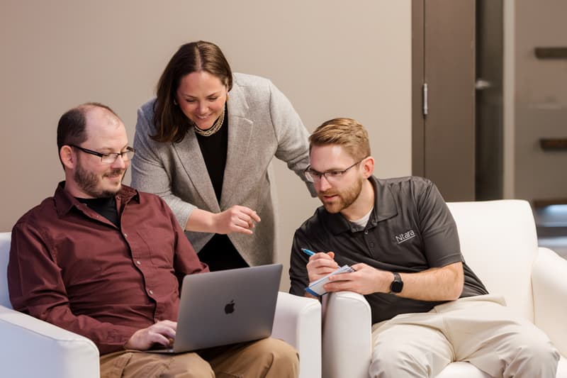 Image of three people, two men and one woman, circled around a computer, talking.