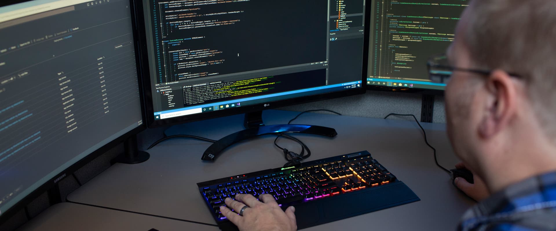 Man at computer typing on colorful keyboard with three screens of code in front of him
