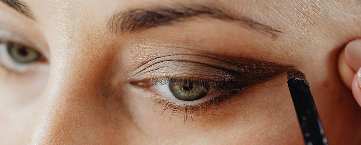 Close-up of a person applying brown eyeshadow with a brush to their eyelid.